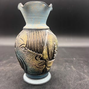 May include: A small, blue and brown ceramic vase with a floral design. The vase has a scalloped rim and a textured surface.