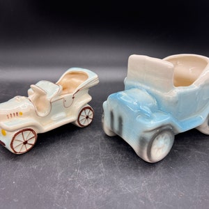 May include: Two vintage ceramic car planters. One is white with brown accents and the other is blue with brown and white accents.