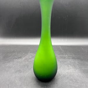 May include: A green glass vase with a rounded bottom and a narrow neck. The vase is frosted and has a gradient of color from a lighter green at the top to a darker green at the bottom.