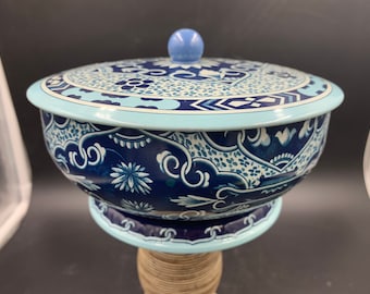 May include: A blue and white porcelain-style tin with a lid. The tin has a floral design and a blue knob on the lid.