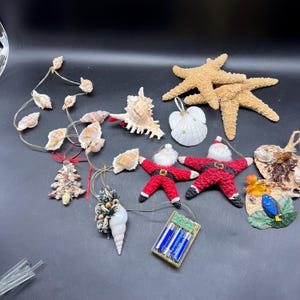 May include: A collection of Christmas ornaments featuring seashells, starfish, and Santa Claus figures. The ornaments are strung on a wire with a battery pack for lights.