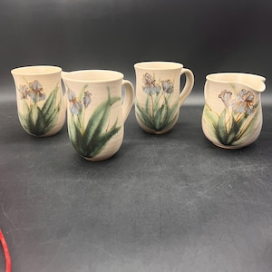 May include: Set of four ceramic mugs with a floral design. The mugs are beige with a green and blue floral pattern. There is also a matching creamer.