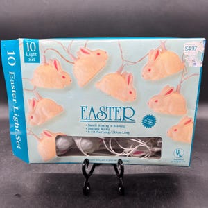 May include: A box of 10 white Easter bunny shaped string lights with pink accents. The lights are 9 1/2 feet long and can be used for indoor or outdoor use. The box says "Easter" and "10 Light Set".