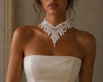 May include: A white strapless bodice paired with an intricate, wide choker necklace featuring dense white beadwork and small pearl accents in a symmetrical, ornate pattern that tapers to a single teardrop pearl at the center of the neckline.