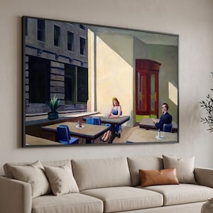 Puede incluir: Una impresión de arte mural enmarcada que representa una escena de café urbano con una persona con vestido azul sentada en una mesa y otra con traje oscuro en una mesa separada, con fachadas de edificios e iluminación cálida.