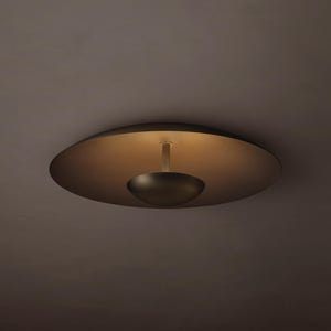 May include: A dark brown flush mount ceiling light fixture featuring a large, flat, circular disc base and a smaller, bowl-shaped shade suspended by a central rod. The design creates a soft, warm glow reflecting off the interior surface.