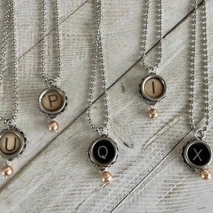 May include: Seven silver necklaces with typewriter key pendants and pearl accents. The keys spell out the letters U, P, Q, I, X, and Y.