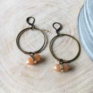 May include: A pair of gold hoop earrings with a peach-colored crystal pendant hanging from each hoop.