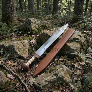 May include: A double-edged sword with a polished steel blade, a light-colored spiraled grip, and a dark wood pommel. Beside the sword lies a smooth, brown leather scabbard. The sword features a wide, leaf-shaped blade design with a central ridge.
