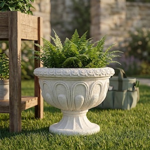 May include: A white stone-look pedestal planter with a wide, rounded bowl featuring a textured, scalloped relief pattern around the exterior and a decorative rim, containing a lush, vibrant green fern plant with delicate, feathery fronds.