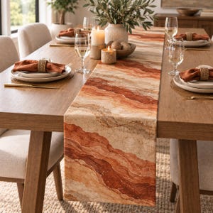 May include: A long rectangular table runner featuring a wavy, layered pattern in shades of terracotta, burnt orange, cream, and beige. The fabric displays a textured, stone-like aesthetic with flowing horizontal bands that span the length of the runner.