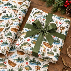 May include: A rectangular gift box wrapped in white paper featuring a repeating pattern of fish, wooden boats, fishing rods, lures, and tackle boxes, tied with a wide olive green satin ribbon. A matching roll of wrapping paper sits beside it.