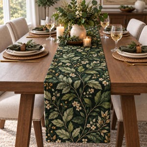 May include: A long rectangular table runner featuring a dark green background with a repeating botanical pattern of light green leaves, small white flowers, and golden berries, draped down the center of a wooden dining table with place settings.