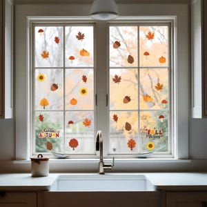 May include: A set of autumn-themed window decals applied to a double-pane window. The stickers feature colorful illustrations of pumpkins, sunflowers, pinecones, mushrooms, and various fall leaves, with text reading hello AUTUMN and FALL VIBES.