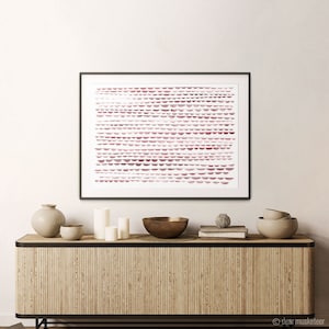 May include: A framed abstract art print with a geometric pattern of pink and white semi-circles. The print is hanging on a white wall above a wooden shelf with decorative bowls and candles.