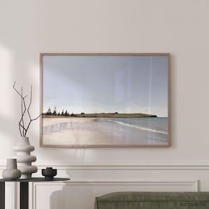 Può includere: Una stampa incorniciata di un paesaggio costiero. L'opera d'arte raffigura una spiaggia sabbiosa, dolci onde e una massa di terra distante sotto un cielo nuvoloso. La cornice è in legno chiaro, che completa i toni naturali della scena.