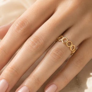 May include: A gold ring featuring a repeating openwork honeycomb pattern. The band is constructed from interconnected hexagonal shapes, creating a delicate and geometric design that encircles the finger with a polished metallic finish.