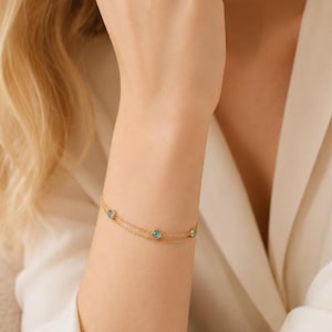 May include: A delicate gold chain bracelet featuring two thin, parallel strands connected by three small, round, bezel-set light blue gemstones spaced evenly along the length of the chain, creating a layered appearance on the wrist.