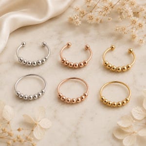 Peut inclure: Six bagues disposées sur deux rangées, comprenant trois anneaux ouverts et trois anneaux fermés. Chaque bague est ornée de cinq petites perles métalliques polies. La collection présente des finitions en métal argenté, doré rose et doré.