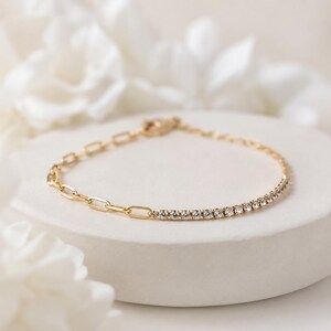 May include: A gold-toned bracelet featuring a dual-design chain. One half consists of elongated oval links, while the other half is a delicate row of small, clear, round-cut stones set in a continuous line, creating a refined and balanced aesthetic.