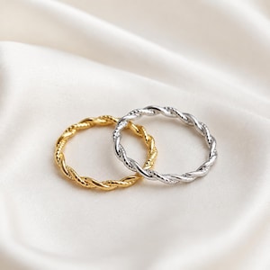Puede incluir: Dos anillos finos con textura de cuerda trenzada. Un anillo tiene un acabado en tono dorado brillante, mientras que el otro anillo tiene un acabado en tono plateado pulido. Ambos anillos presentan un diseño en espiral uniforme y continuo.