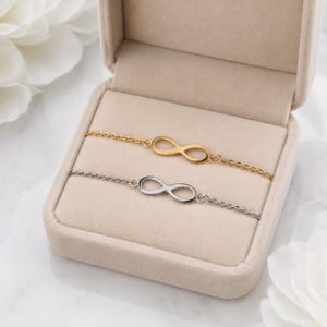 Peut inclure: Deux bracelets à chaîne délicats dotés d'un symbole infini central. L'un des bracelets présente une finition dorée polie, tandis que l'autre présente une finition argentée polie. Les deux bracelets sont présentés dans un écrin en velours beige.