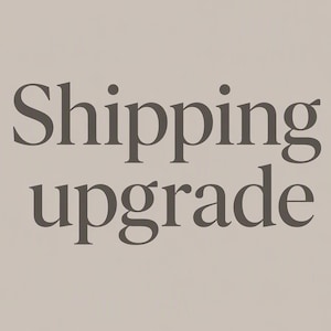 Op de afbeelding: Een lichtbeige achtergrond met de tekst Shipping upgrade in een donkerbruin schreeflettertype. De tekst is gecentreerd en beslaat het middelste gedeelte van het kader, gepresenteerd in een duidelijke, leesbare en professionele stijl.