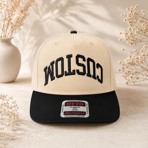 Könnte beinhalten: Eine beige Baseballkappe mit schwarzem Schirm und schwarzem, bogenförmig gesticktem Schriftzug CUSTOM. Die Kappe hat einen schwarzen Knopf oben und einen rechteckigen Aufkleber auf dem Schirm mit dem Text OTTO, CLASSIC FIT, OSFM, MID PROFILE.