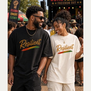 May include: A black t-shirt and a cream t-shirt, both featuring the word Resilient in a gold cursive font above a horizontal brushstroke graphic in red, yellow, and green colors. The shirts have short sleeves and a crew neckline design.