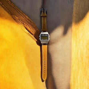 Peut inclure: Une montre-bracelet numérique dotée d'un boîtier rectangulaire argenté avec un écran d'affichage noir et un bracelet en cuir jaune moutarde avec des surpiqûres blanches. La montre comprend une boucle en métal et des trous de réglage.