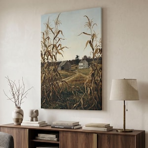 Peut inclure: Une impression d'art mural rectangulaire représentant un paysage rural avec de hauts plants de maïs séchés au premier plan encadrant un chemin de terre menant à une ferme blanche et une grange en bois sous un ciel pâle, aux tons terreux.