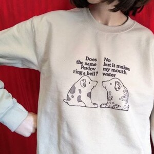 May include: A light beige sweatshirt with a graphic of two dogs and the text "Does the name Pavlov ring a bell? No but it makes my mouth water."