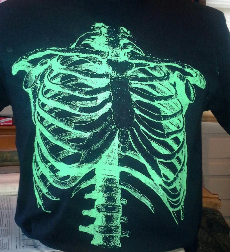 Puede incluir: Una camiseta negra con un estampado de costillas de esqueleto verde que brilla en la oscuridad.