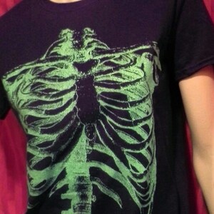 Puede incluir: Camiseta negra con un gr&aacute;fico de esqueleto verde que brilla en la oscuridad en la parte delantera.