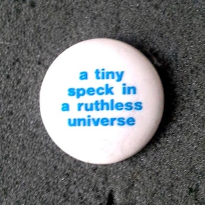 Ongedragen retro jaren 80-knoop "A tiny speck in a ruthless universe" (een klein stipje in een meedogenloos universum), in zo goed als nieuwe staat, diameter 2,5 cm (vrij klein)
