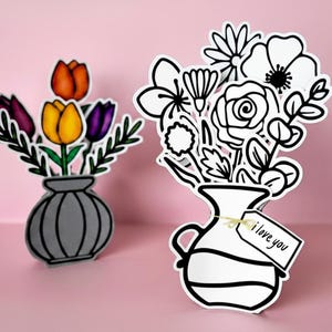 May include: Two paper flower bouquet cutouts. One features a gray vase with orange, yellow, and purple tulips. The other is a black and white outline of a mixed flower arrangement in a vase with a small tag tied to it that reads I love you.