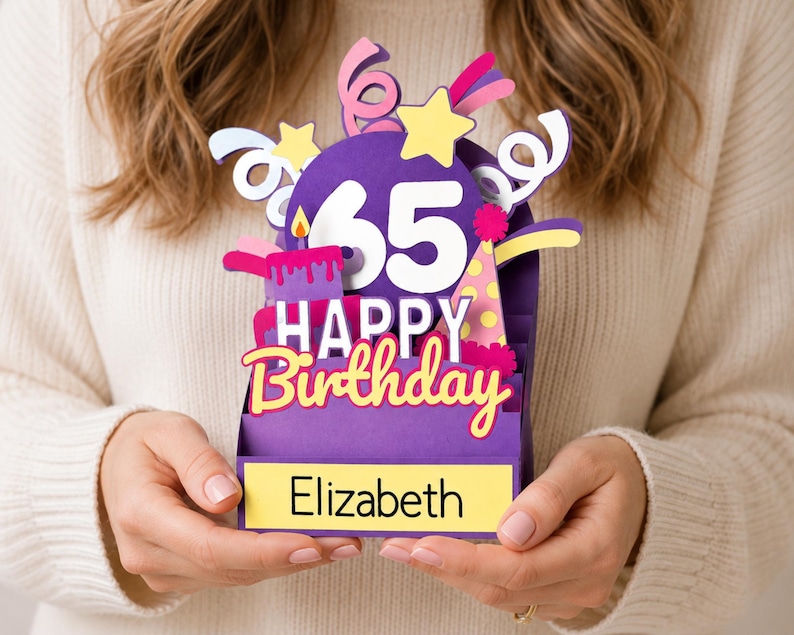 May include: A purple 3D pop-up birthday card featuring the number 65, a lit candle, a party hat, and colorful streamers. The text reads Happy Birthday and Elizabeth on a yellow rectangular base. The design includes yellow stars and pink accents.