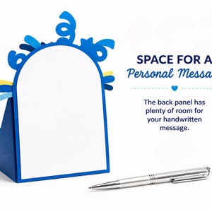 May include: A blue arched card with a white center panel and blue confetti-like cutouts at the top. The text reads: SPACE FOR A PERSONAL MESSAGE. The back panel has plenty of room for your handwritten message. A silver ballpoint pen lies in front.