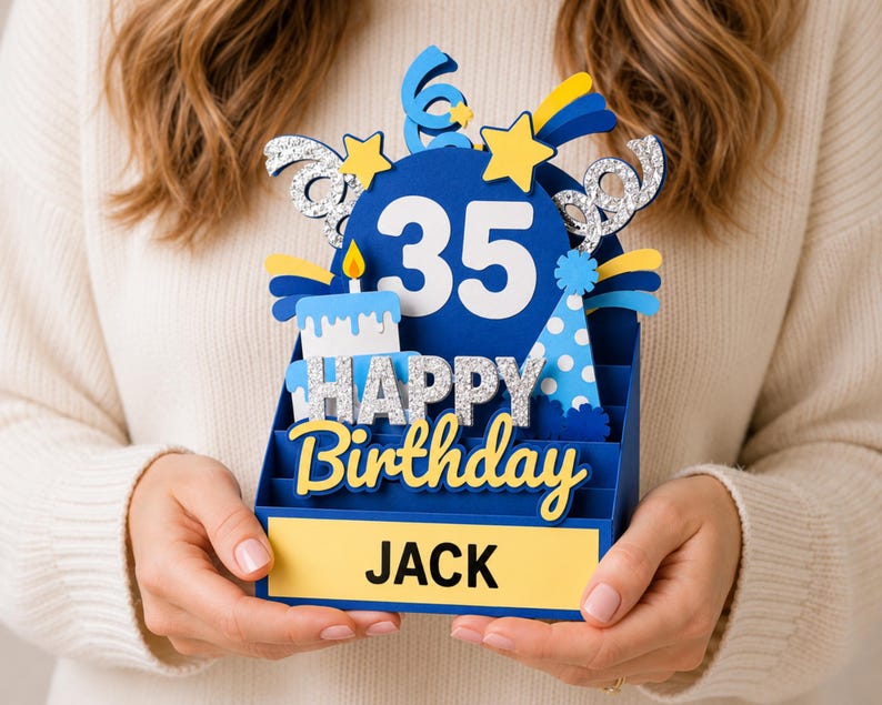 May include: A three-dimensional blue birthday card featuring the number 35, a cake, and a party hat. The card displays the text HAPPY BIRTHDAY in silver glitter and the name JACK in black letters on a yellow rectangular base with star accents.
