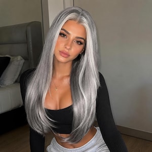 May include: A long, straight wig featuring a blend of silver and grey tones with a distinct white money piece framing the face. The hair is parted in the center, falling past the shoulders in smooth, layered strands with a natural-looking hairline.