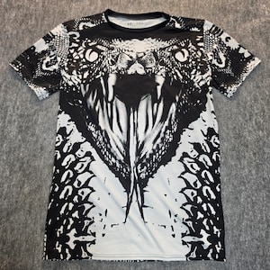 May include: A short-sleeve crew neck t-shirt featuring a high-contrast black and white graphic print of a snake head with an open mouth and visible fangs. The pattern extends across the entire front of the garment, showcasing detailed scales.