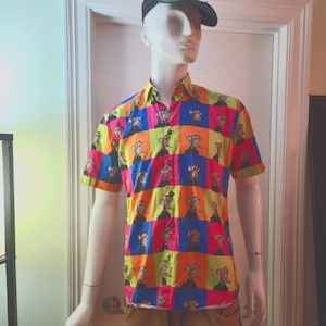 May include: A short-sleeved button-down shirt featuring a vibrant grid pattern of alternating blue, pink, orange, and lime green squares. Each square contains a repeating graphic illustration of a cartoon monkey character wearing a dark hoodie.