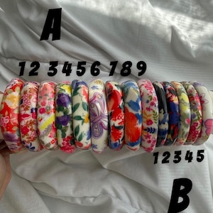 Op de afbeelding: Een collectie van veertien armbanden op een rij, elk met verschillende kleurrijke bloemen-, vlinder- of abstracte patronen. De armbanden zijn gelabeld met de letters A en B en de cijfers 1 tot en met 9 en 1 tot en met 5.