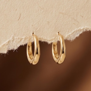 Puede incluir: Un par de pequeños aros de oro pulido con una superficie lisa y redondeada. Los pendientes tienen forma circular y presentan un acabado metálico reflectante que capta la luz, mostrando un diseño sencillo y limpio para el uso diario.