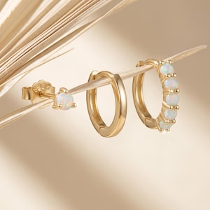 May include: A set of three gold-toned earrings featuring one stud earring with a single round opal, one plain gold hoop earring, and one gold hoop earring accented with five small round opals. Each piece is stamped with S925.