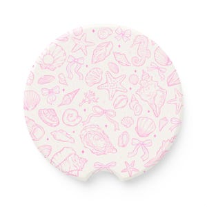 May include: A circular car coaster with a white background and a repeating pattern of light pink line art illustrations featuring various seashells, starfish, seahorses, small bows, and tiny four-pointed stars across the entire surface.