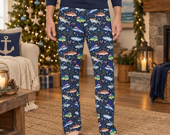 Puede incluir: Pantalones de pijama azul marino con un patrón repetitivo de varios peces con gorros de Papá Noel rojos y blancos, intercalados con pequeñas hojas de acebo verdes y bayas rojas sobre un fondo azul oscuro con copos de nieve.