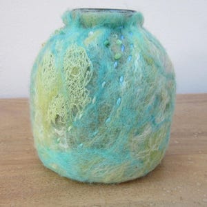 May include: A rounded vase covered in textured, felted wool in shades of turquoise, light blue, and lime green. The surface features intricate, raised fibre patterns and small, scattered beads in matching blue and green tones.