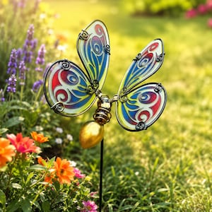 Peut inclure: Une décoration de jardin en forme de papillon avec des ailes translucides aux tons rouge, bleu et jaune, bordées de fil noir. Le corps du papillon se compose d'une forme ovale métallique dorée et d'une section en fil torsadé sur une tige.