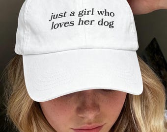 以下が含まれることがあります： フロントパネルの中央に「just a girl who loves her dog」という黒い刺繍が施された白い野球帽。この帽子は、構造化されたクラウン、カーブしたつば、上部のボタンが特徴で、すっきりとシンプルなデザインに仕上がっています。